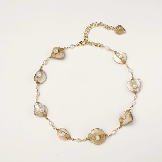 Gold-plated necklace with wire-wrapped shell pieces and freshwater pearls on neutral background, adjustable chain visible.