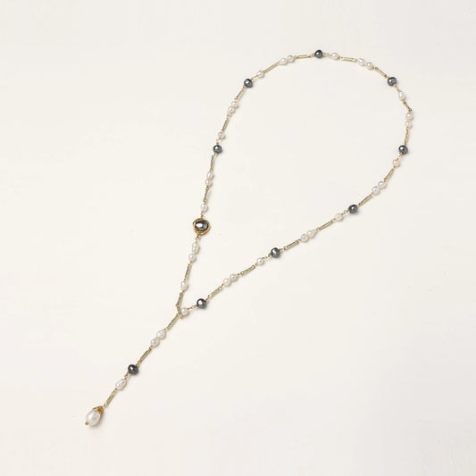 Y-shaped gold-plated necklace with white and gray freshwater pearls on cream background, showing adjustable drop design.