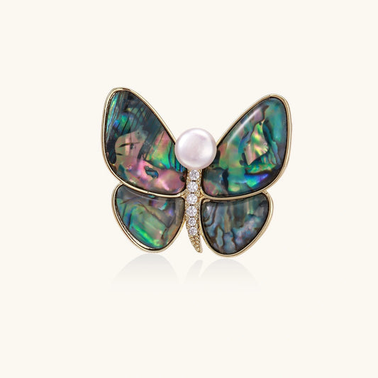 Gold-plated butterfly brooch with iridescent abalone shell wings and freshwater pearl accent on cream background.