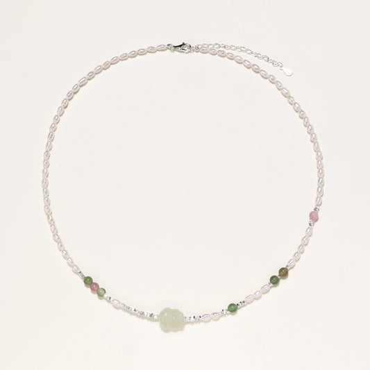 Delicate pearl necklace with pale green serpentine jade centerpiece and colorful agate beads on cream background
