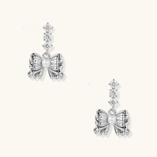 White gold plated drop earrings with three graduated zirconia crystals leading to a bow charm with pearl center