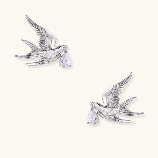 Silver-toned swallow stud earrings with detailed wings carrying teardrop zirconia crystals on white background