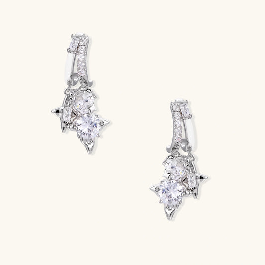 White gold-plated huggie earrings with geometric emerald-cut zirconia clusters in starburst formation on beige background