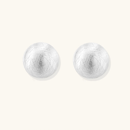 Brushed sterling silver half-dome clip-on earrings with textured surface against cream background