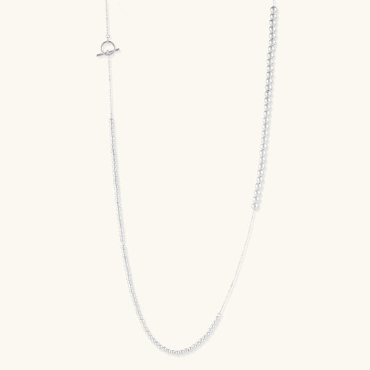 Long sterling silver beaded necklace with graduated sphere design, toggle clasp, and delicate chain extension on white background