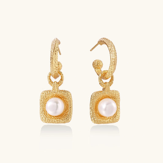 Pair of gold vermeil hoop earrings with textured square frames holding freshwater pearls on cream background