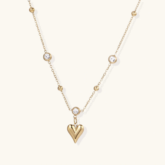 Delicate gold-plated necklace with bezel-set crystals and small heart pendant on beige background