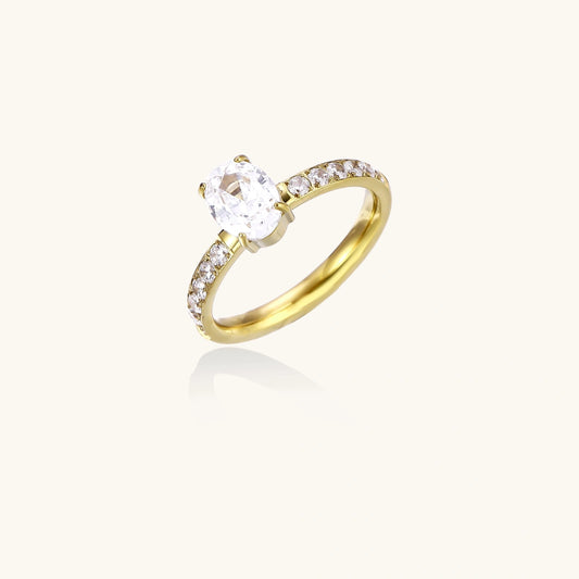 Gold-plated solitaire ring with oval zirconia center stone and pavé band on cream background