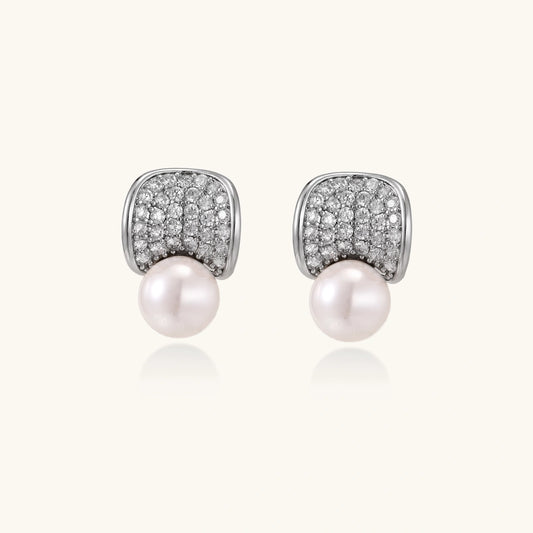 Curved pavé diamond studs in white gold-plated brass cradle lustrous freshwater pearls against cream background