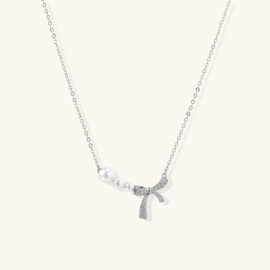 Delicate white gold plated necklace with freshwater pearls and sparkly crystal bow pendant on white background