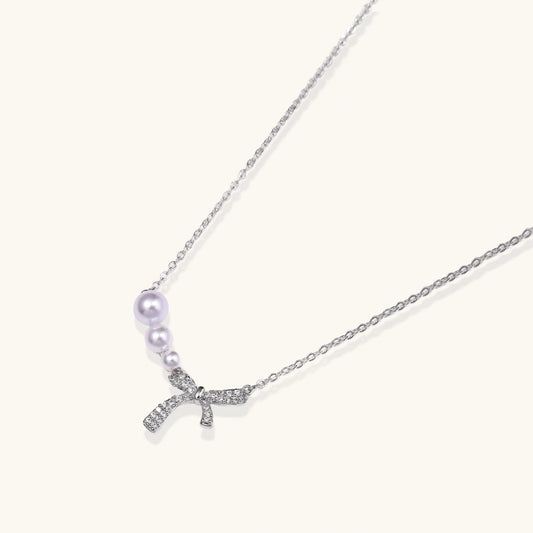 Delicate white gold plated necklace with freshwater pearls and sparkly crystal bow pendant on white background