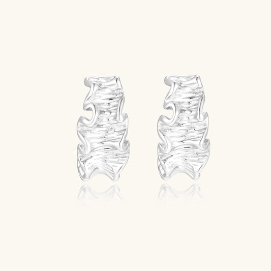 White gold plated sculptural hoop earrings with organic wavy edges and reflective metallic finish on cream background