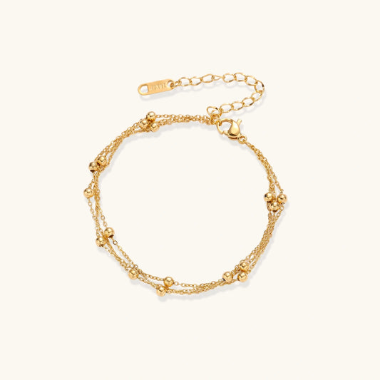 Three-strand gold-plated bracelet with clustered ball beads and adjustable clasp on cream background