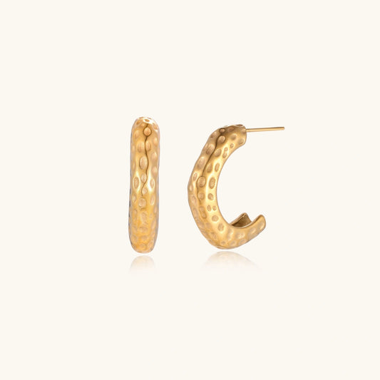 Gold-toned hoop earrings with hammered dimpled texture and post closure on cream background