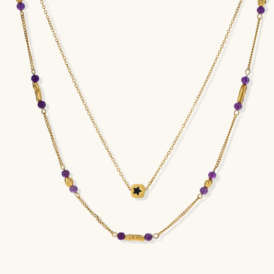 Two layered gold-tone necklaces with purple stone beads and star pendant against cream background.