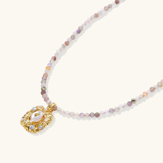 Ornate gold-plated pendant necklace with multicolored gemstone beads in purple, pink and clear tones on white background