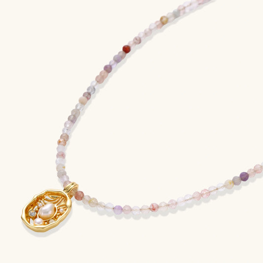 Delicate gold-plated necklace with mixed gemstone beads and ornate oval pendant on white background