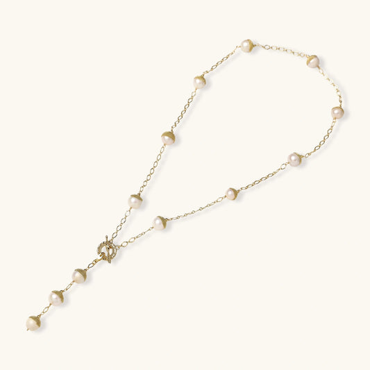 Gold-plated lariat necklace with baroque pearls and textured caps on cream background, showing adjustable Y-shaped design.