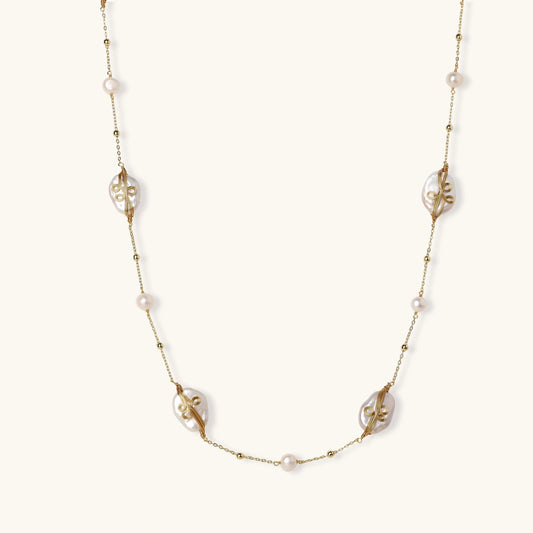 Long gold chain necklace with baroque pearls wrapped in leaf designs and small freshwater pearls spaced along the strand
