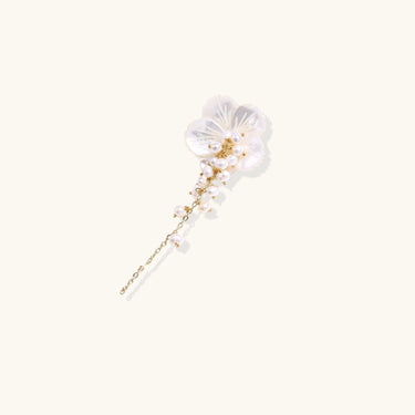 Iridescent shell flower brooch with carved petals and cascading freshwater pearls on gold chain against cream background.