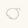 Rhodium-plated silver chain bracelet with single white freshwater pearl and heart charm clasp on cream background