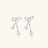 Rhodium-plated silver earrings with organic vine curves and two peachy freshwater pearls on cream background
