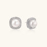 Rhodium-plated sterling silver stud earrings with round freshwater pearls surrounded by geometric crystal halos on cream background.