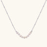Delicate sterling silver chain necklace with small freshwater pearls arranged in a curved smile arc on cream background.