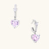 Silver huggie hoops with pink heart-cut zirconia pendants on white background, eco-friendly white gold plated brass