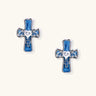 White gold-plated cross earrings with blue enamel, bat wing details, and heart-shaped zirconia center on cream background.