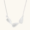 Minimalist sterling silver necklace with three brushed leaf-shaped pendants on delicate chain against white background