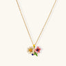 Enamel floral pendant necklace with white daisy, pink flower, yellow and blue accents on gold chain against cream background.