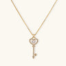Delicate gold key pendant with heart-shaped bow and crystal pavé detailing on fine chain against cream background.