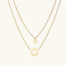 Gold layered necklace set with sunburst and smiley face pendants on delicate chains against white background.