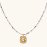 Ornate gold-plated pendant necklace with multicolored gemstone beads in purple, pink and clear tones on white background