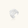Wide sterling silver cuff ring with flowing wave patterns creating dimensional texture against cream background